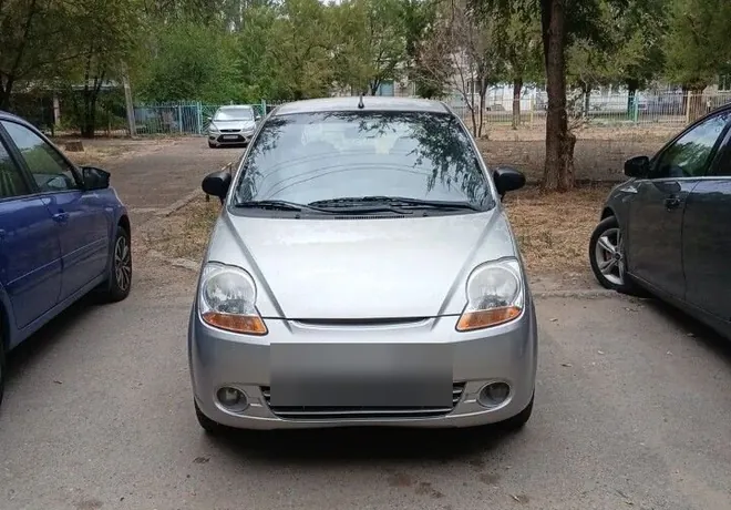 Серебристый компактный Chevrolet Spark, показанный спереди на парковке.