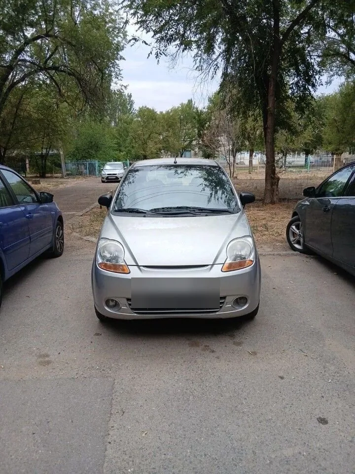 Серебристый компактный Chevrolet Spark, показанный спереди на парковке.