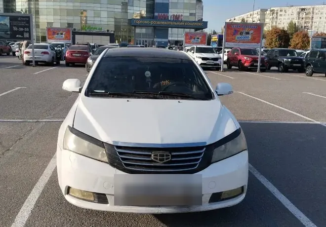 Белый седан Geely на парковке, представлен на фотографии спереди.