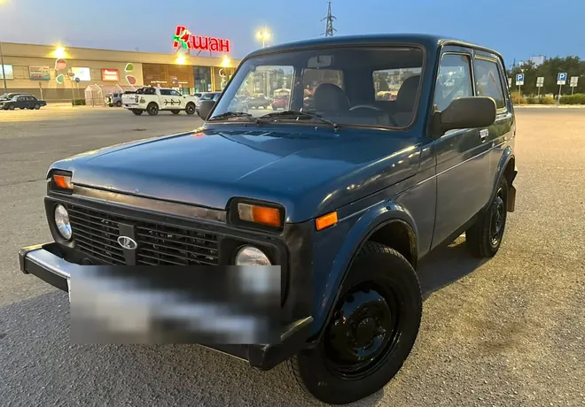 Синяя Lada Niva на парковке, без заметных крупных повреждений передней части.