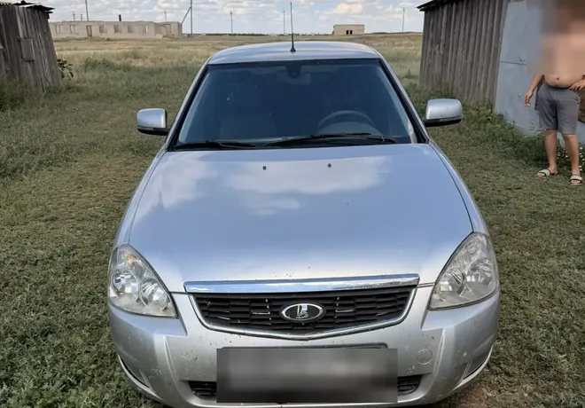 Серебристая Lada Priora на участке, без явных крупных повреждений в переднем ракурсе.