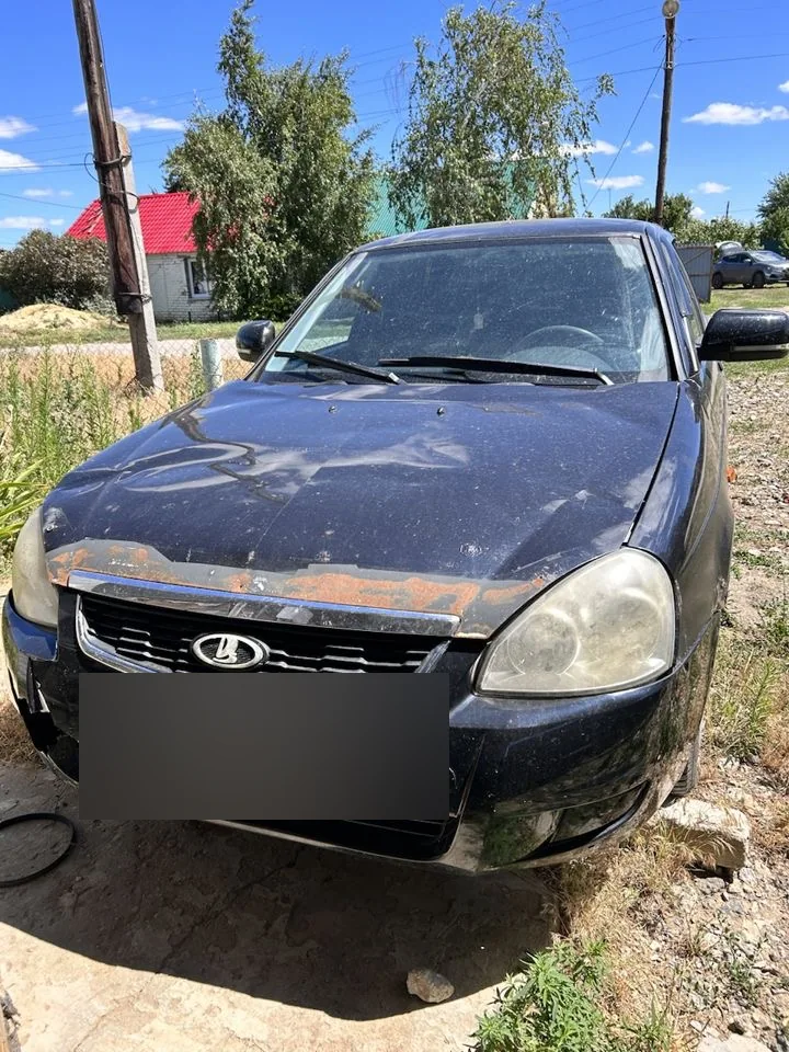 Тёмная Lada Priora; на кромке капота заметны участки с повреждением покрытия и следы ржавчины.